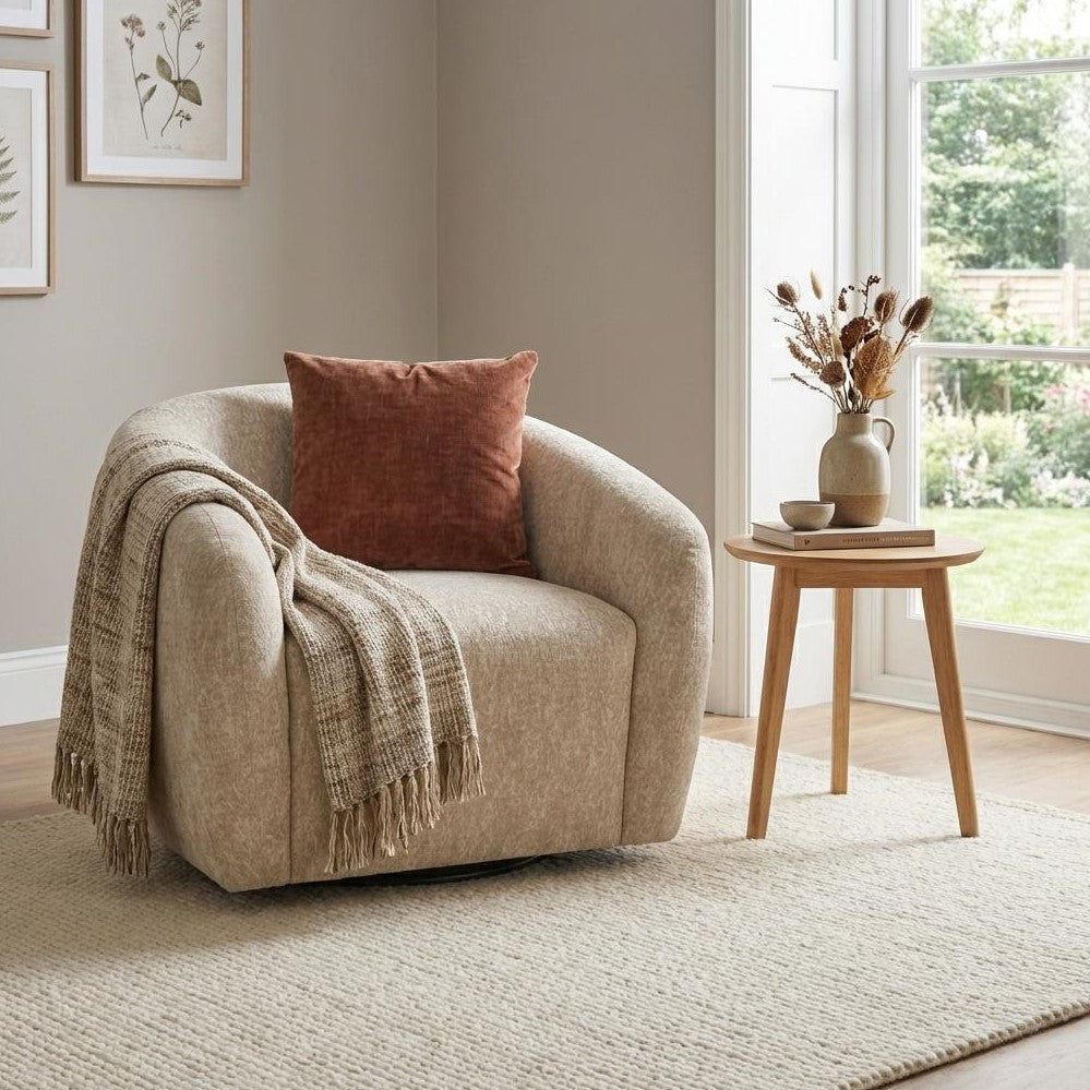 Cozy beige chair with a blanket, pillow, and side table by a window.