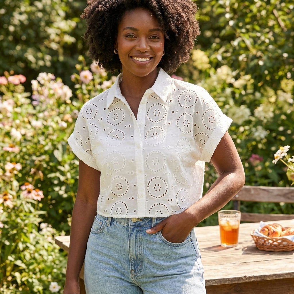 Smiling person in garden, wearing a white eyelet top and jeans, next to a table with snacks.