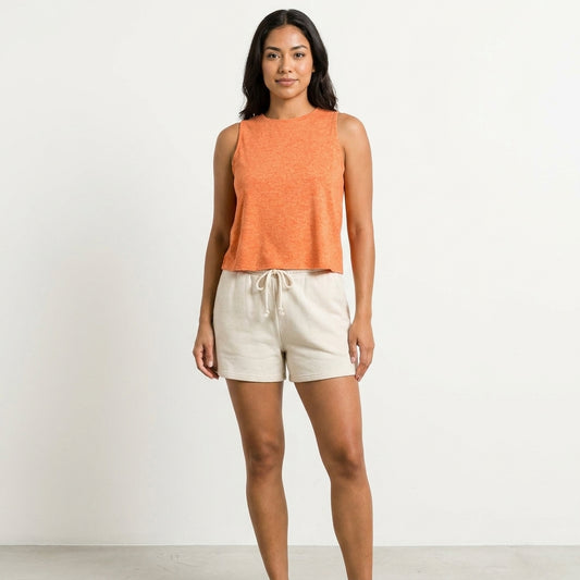 Woman in orange tank top and beige shorts, standing against a plain background.