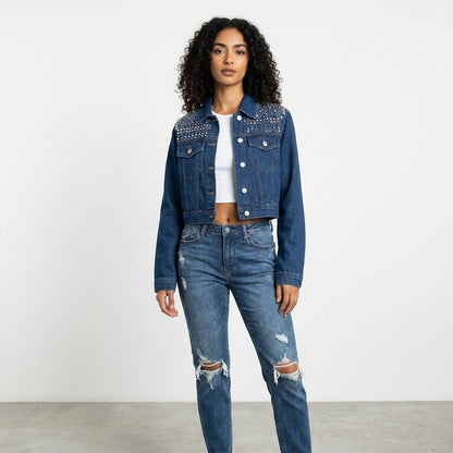 Woman in denim jacket and ripped jeans poses confidently.