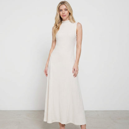Woman in a sleeveless, long beige dress standing against a plain background.