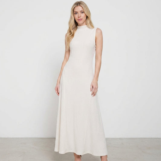Woman in a sleeveless, long beige dress standing against a plain background.