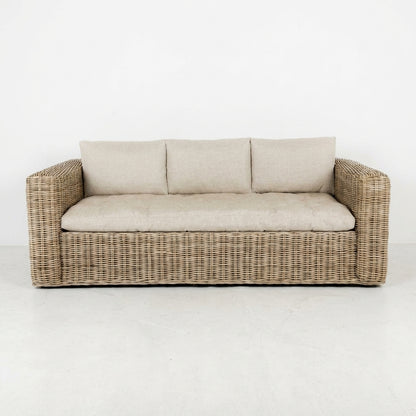 Beige cushioned wicker sofa on white background.