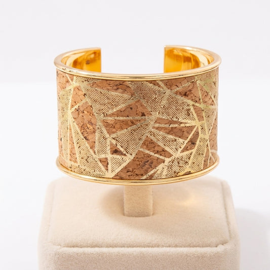 Golden cuff bracelet with geometric cork design on a display stand.