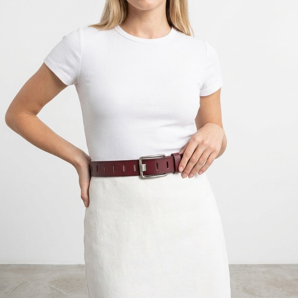 Woman in white outfit with wide brown belt, standing with hands on waist.
