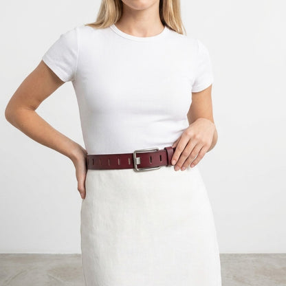 Woman in white outfit with wide brown belt, standing with hands on waist.