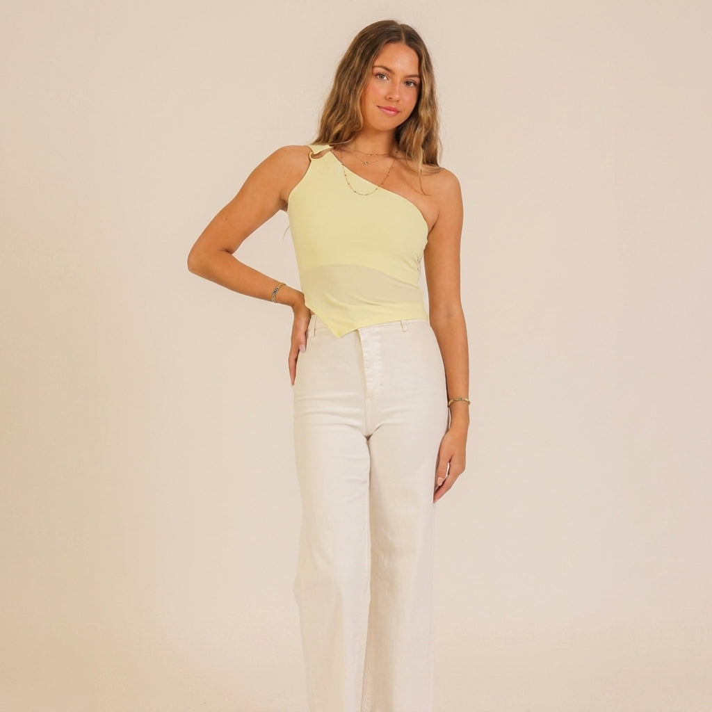 Woman in a yellow one-shoulder top and white pants.