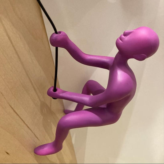 Purple figurine climbing a black rope on a wood surface.