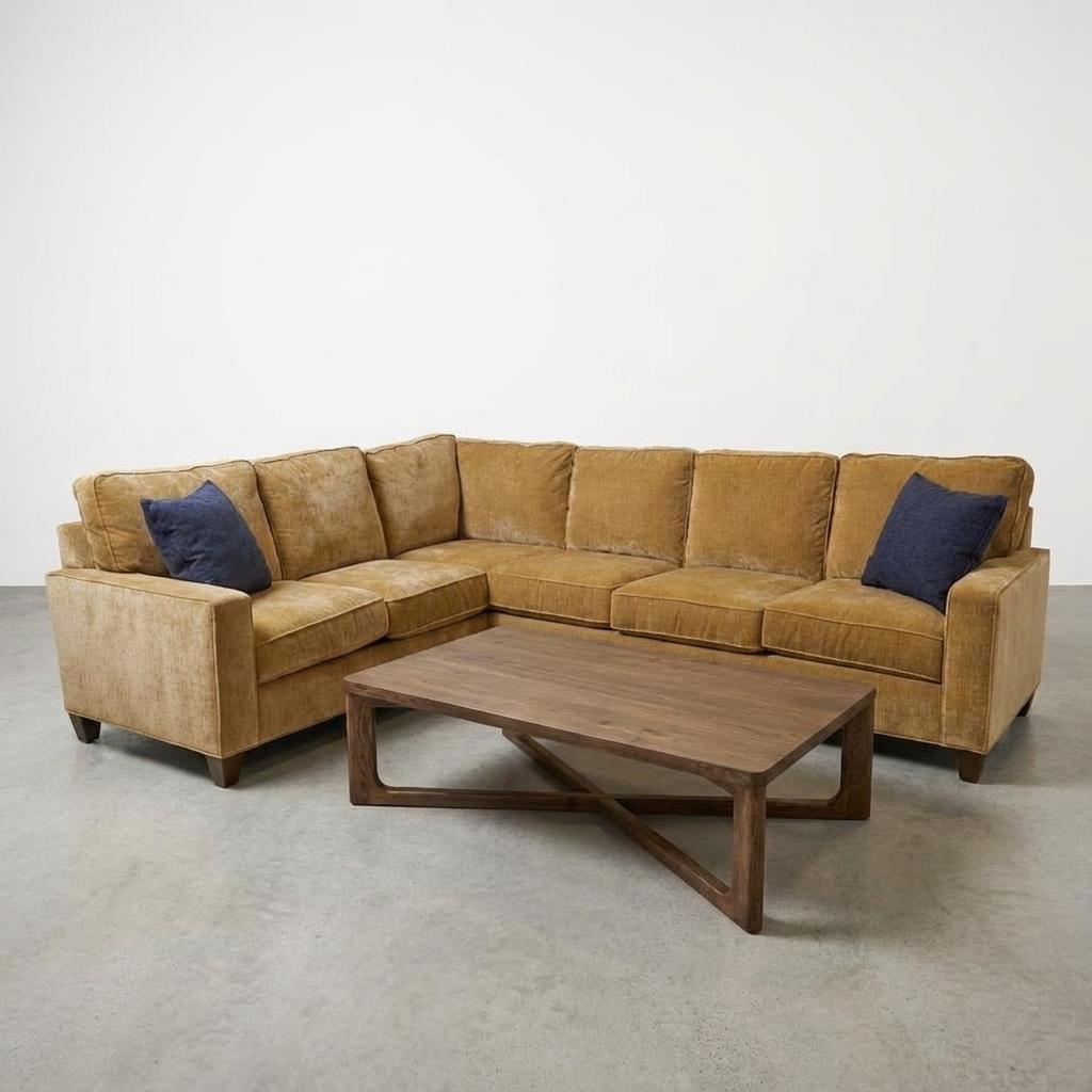 Brown sectional sofa with two navy cushions, and a wooden coffee table on a concrete floor.