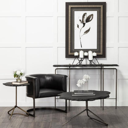 Modern seating area with black chair, tables, candles, and abstract art.