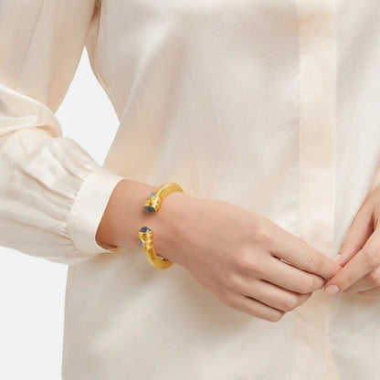 A gold cuff bracelet with blue gemstones worn with an elegant cream blouse.