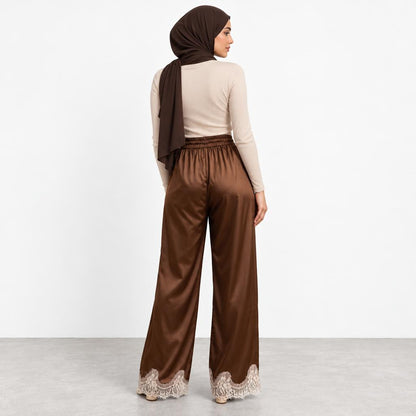 Woman in beige top and brown pants with lace, wearing a matching headscarf.