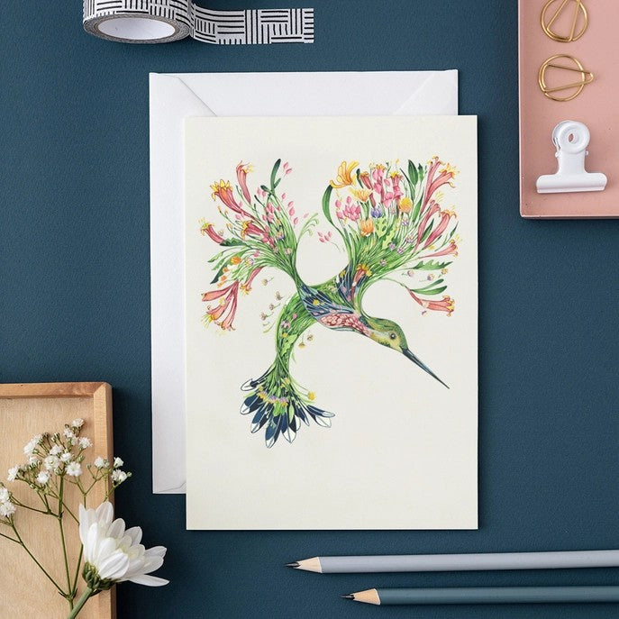 Floral hummingbird card on a desk with pencils and paper clips.