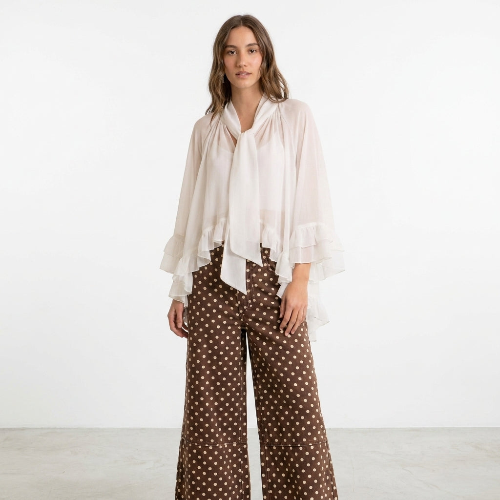Woman in flowy white top and polka dot pants against white background.