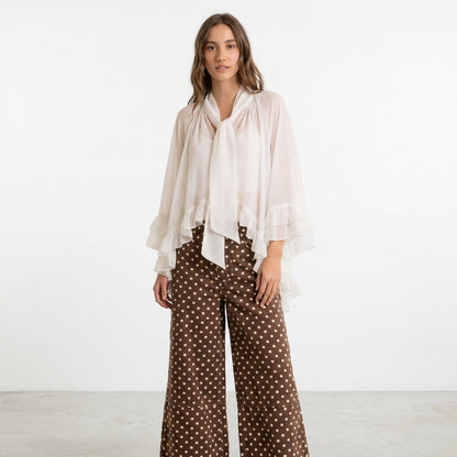 Woman in flowy white top and polka dot pants against white background.