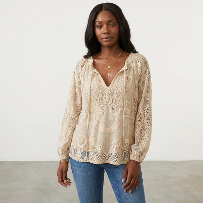 Woman in a lace blouse and jeans, standing against a plain background.