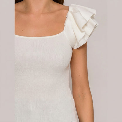 Woman wearing a white top with a ruffled shoulder.