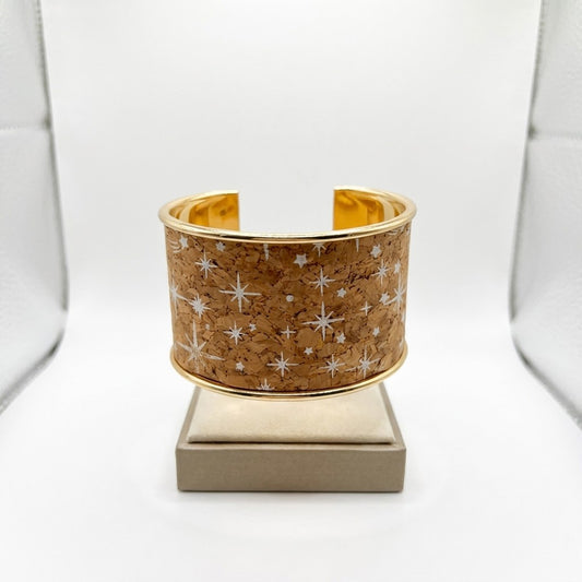 Wide gold bracelet with star pattern on cork backdrop.