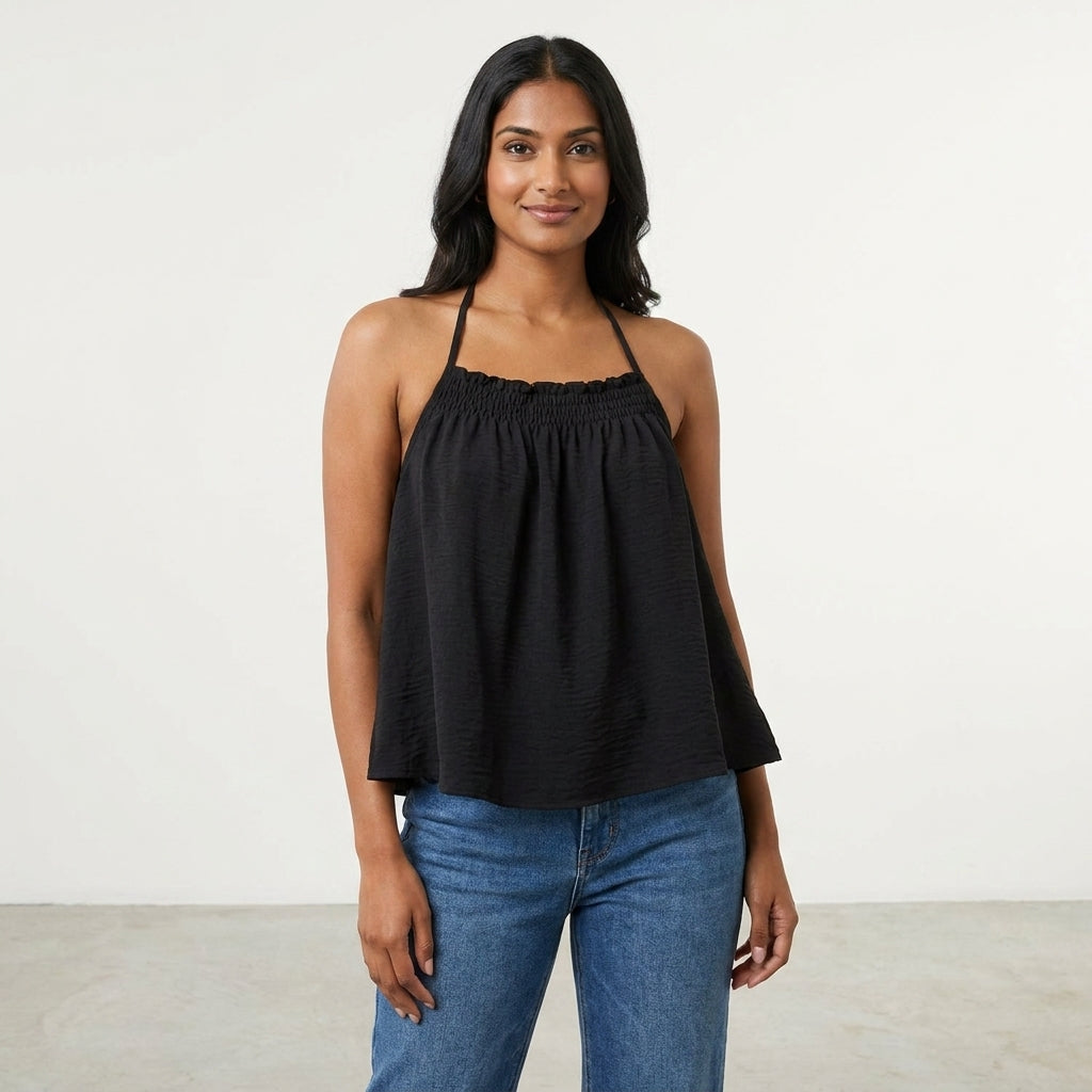 Smiling woman in a black halter top and jeans against a plain background.