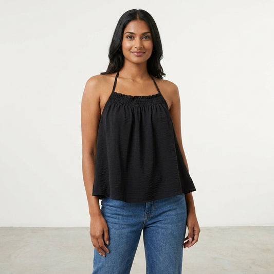 Smiling woman in a black halter top and jeans against a plain background.