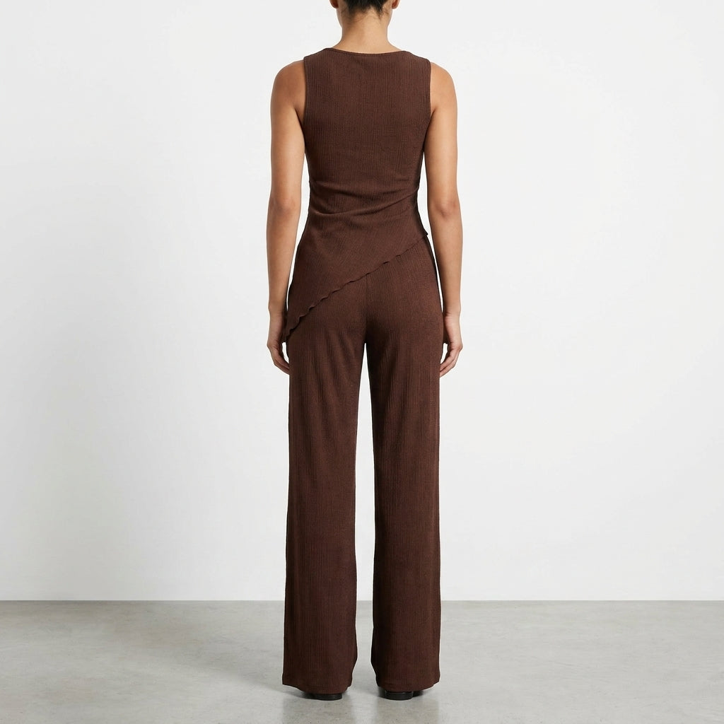 Woman in brown sleeveless jumpsuit, facing away, with simple background.