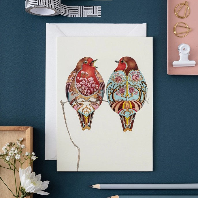 Artistic card with two colorful birds on a branch, surrounded by stationery.
