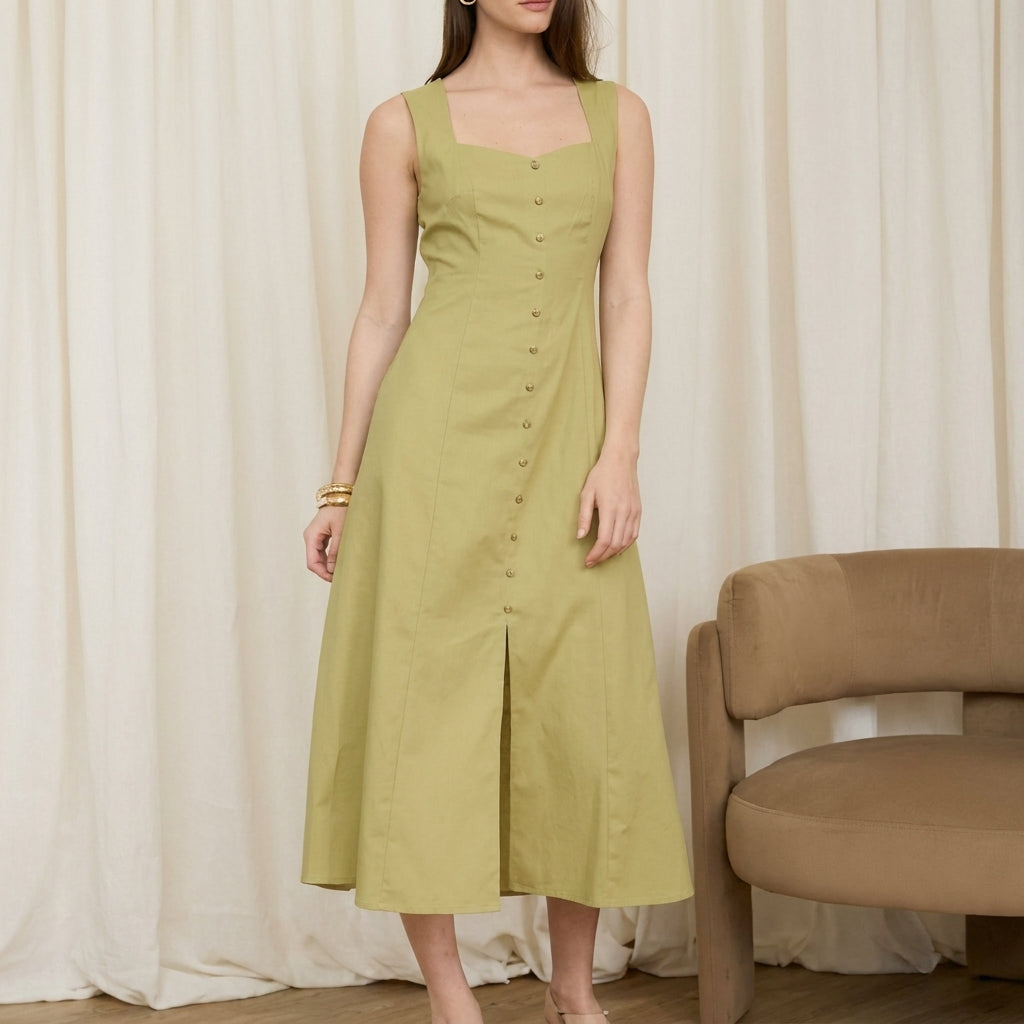 Woman in a buttoned green dress beside a beige chair.
