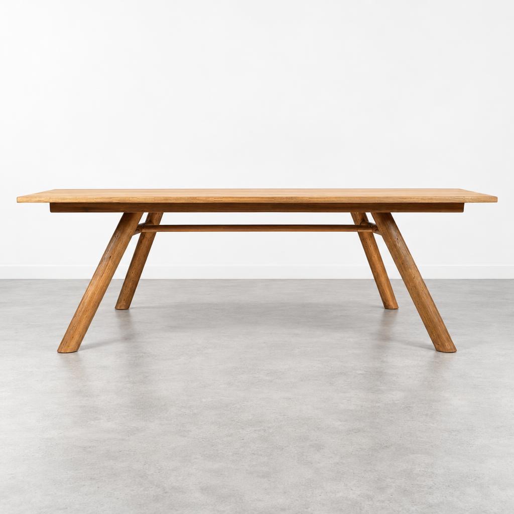A long wooden dining table with angled legs stands in a minimalist room.