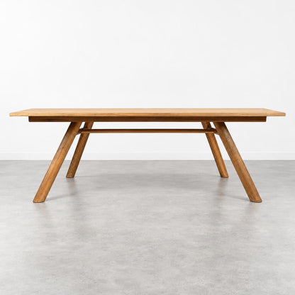 A long wooden dining table with angled legs stands in a minimalist room.