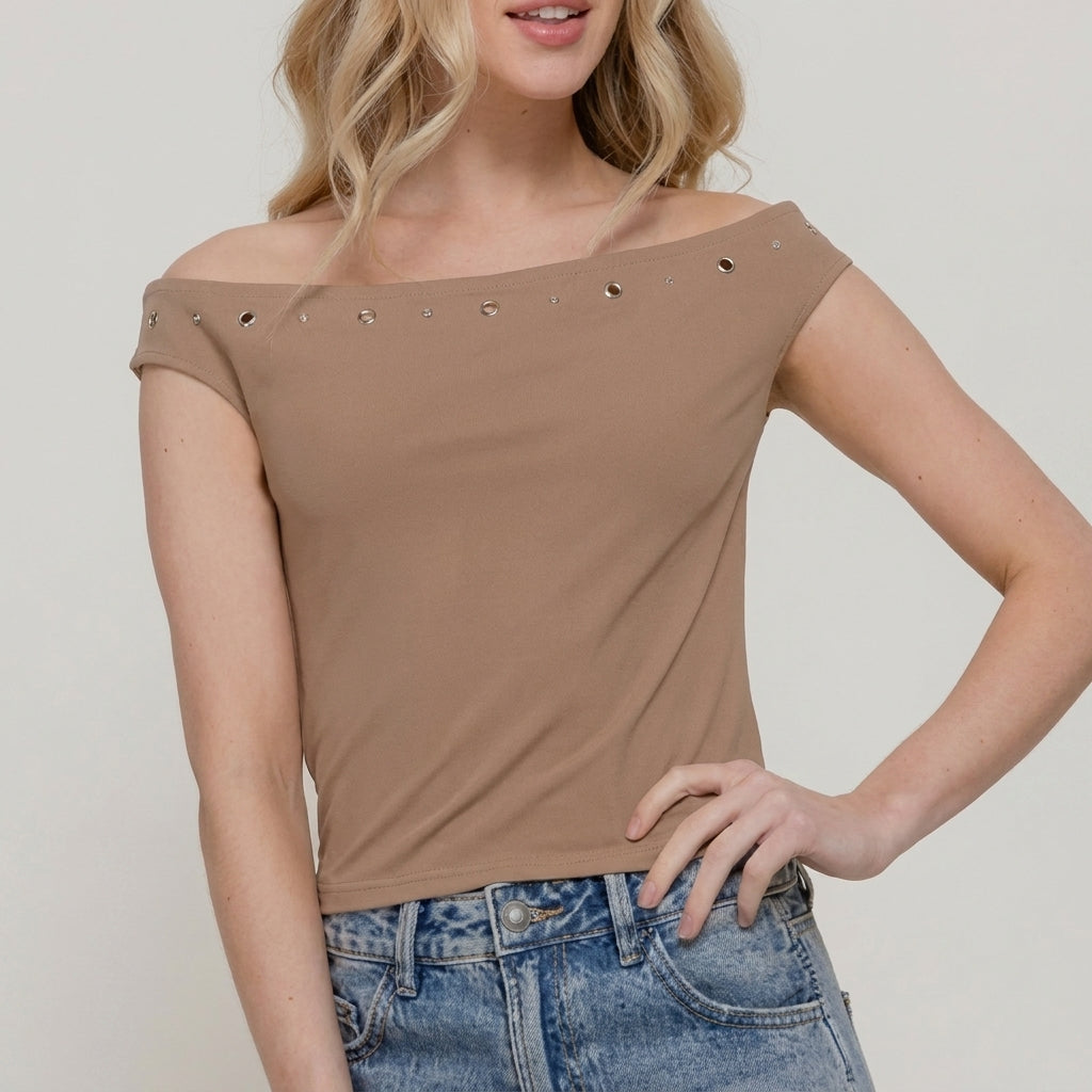 Woman in an off-shoulder beige top and denim jeans against a plain background.