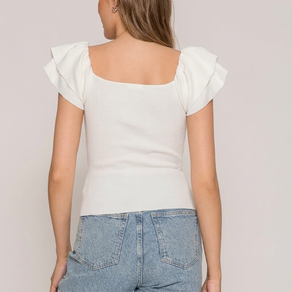 Woman wearing a white top with ruffle sleeves and blue jeans, seen from behind.