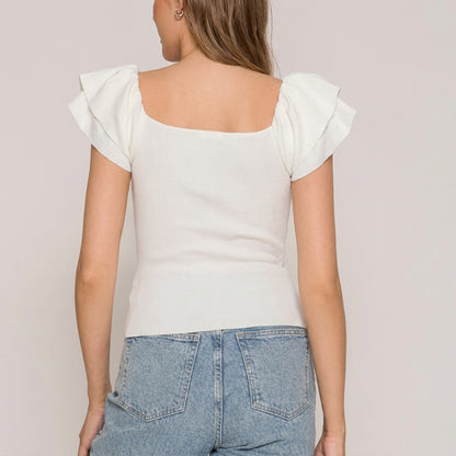 Woman wearing a white top with ruffle sleeves and blue jeans, seen from behind.