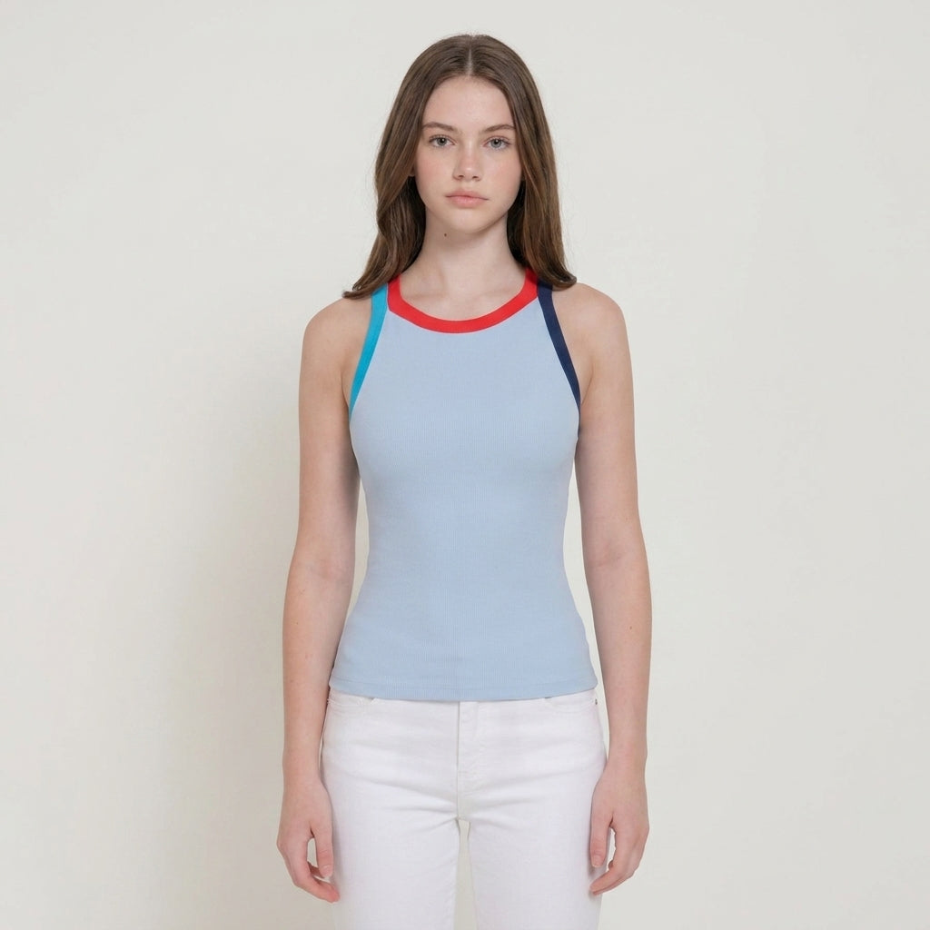 Woman in a blue top with a red neckline, white pants, standing against a plain background.