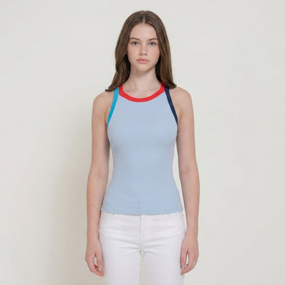 Woman in a blue top with a red neckline, white pants, standing against a plain background.