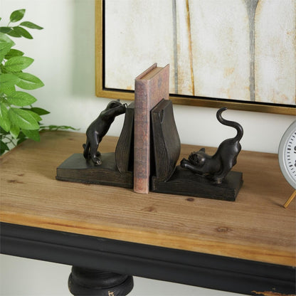 Cat bookends on a wooden table supporting a book, beside a clock and plant.
