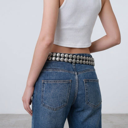 Woman in jeans and white top, wearing a studded belt.