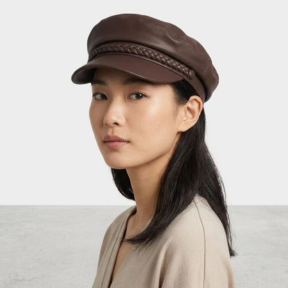 Woman in brown leather cap with braided band, neutral background.