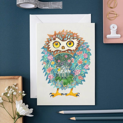 Illustrated owl card on a desk with pencils and flowers.