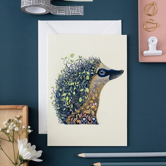 Illustrated hedgehog card with plants, surrounded by stationery items.