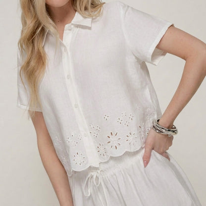 Woman in white floral cut-out top with silver bracelets.