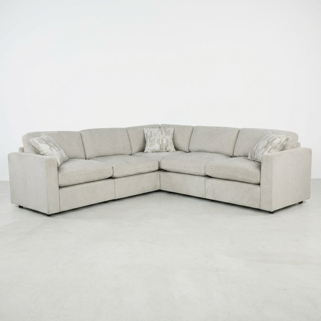 Gray sectional sofa with three patterned cushions on a plain background.