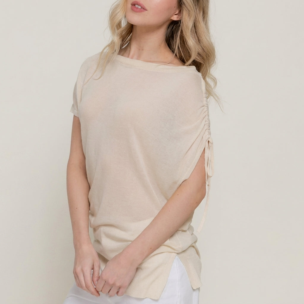 Person in a beige top with ruched sleeve, hands clasped.