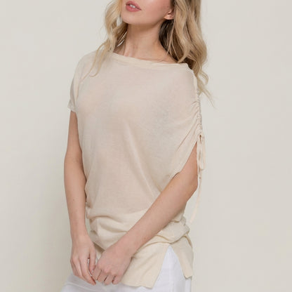 Person in a beige top with ruched sleeve, hands clasped.