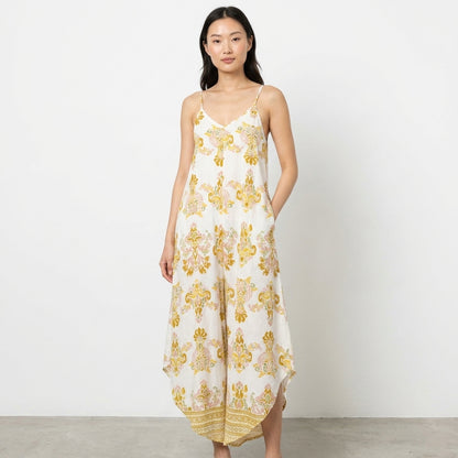 Woman in a floral jumpsuit against a white wall.