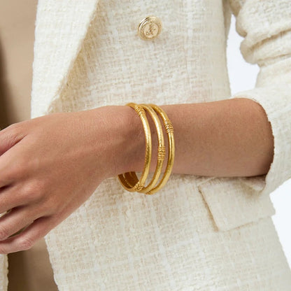 Close-up of a wrist wearing three gold bangles with a cream textured jacket.