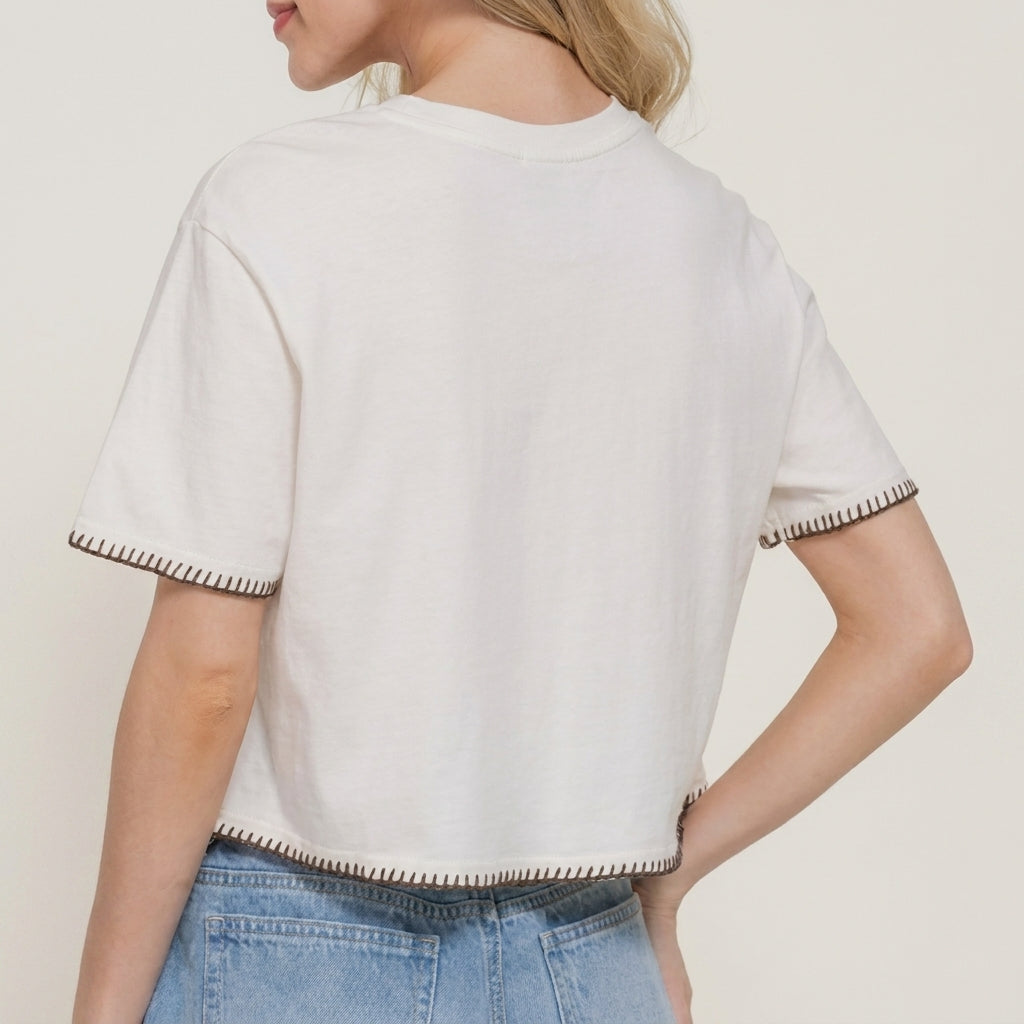 Person wearing a white cropped tee with stitch details and blue jeans, facing away.
