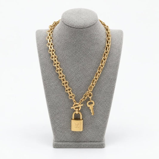 Gold-tone chain necklace with a padlock and key displayed on a gray bust.