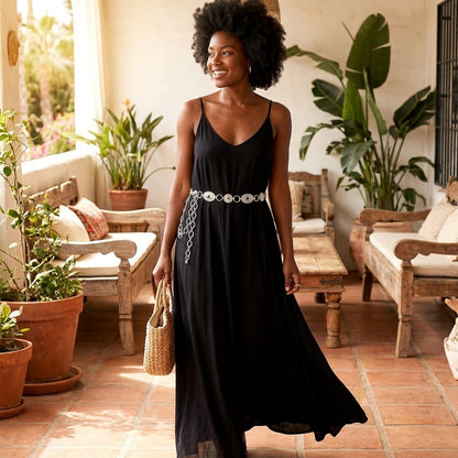 Woman in black dress smiling, standing in a plant-filled room.