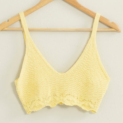 Yellow knit bralette hanging on a wooden hanger.