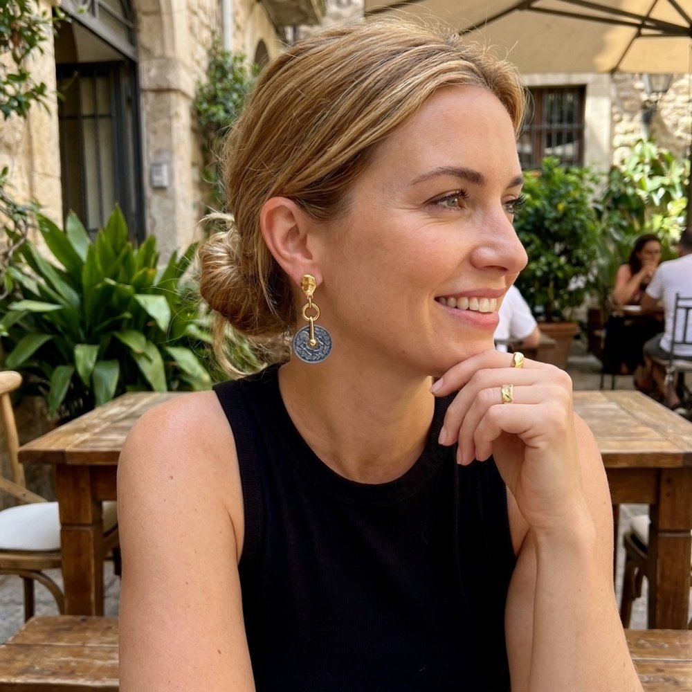 A smiling woman wearing statement earrings sits at an outdoor café.